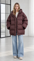 Front view of model wearing oversized hooded chocolate brown puffer jacket with jeans