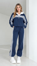 Front full view of woman wearing navy blue striped 2-piece tracksuit set with white hood and sneakers