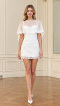 Front full-length view of model wearing white lace capelet mini dress