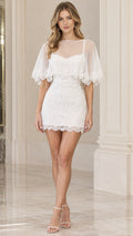 Front view of model wearing white lace mini dress with sheer flutter capelet overlay