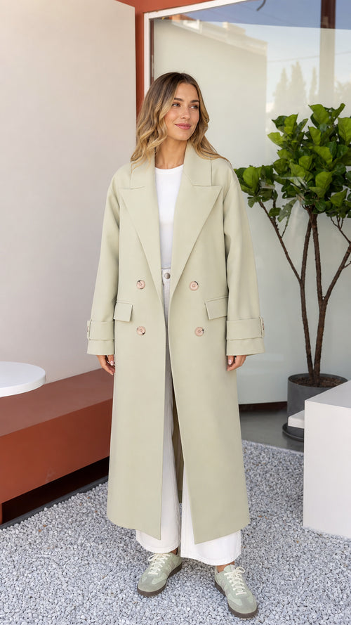 Front full view of woman wearing Sage Green double-breasted maxi trench coat with white wide-leg trousers