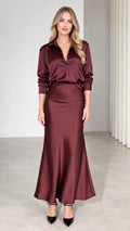Front view of model wearing burgundy satin button-down shirt and matching maxi skirt set