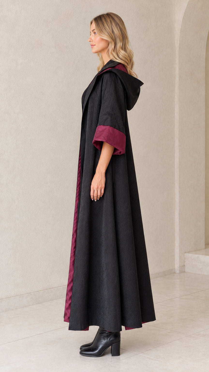 Side profile view of black flowing floor-length hooded coat