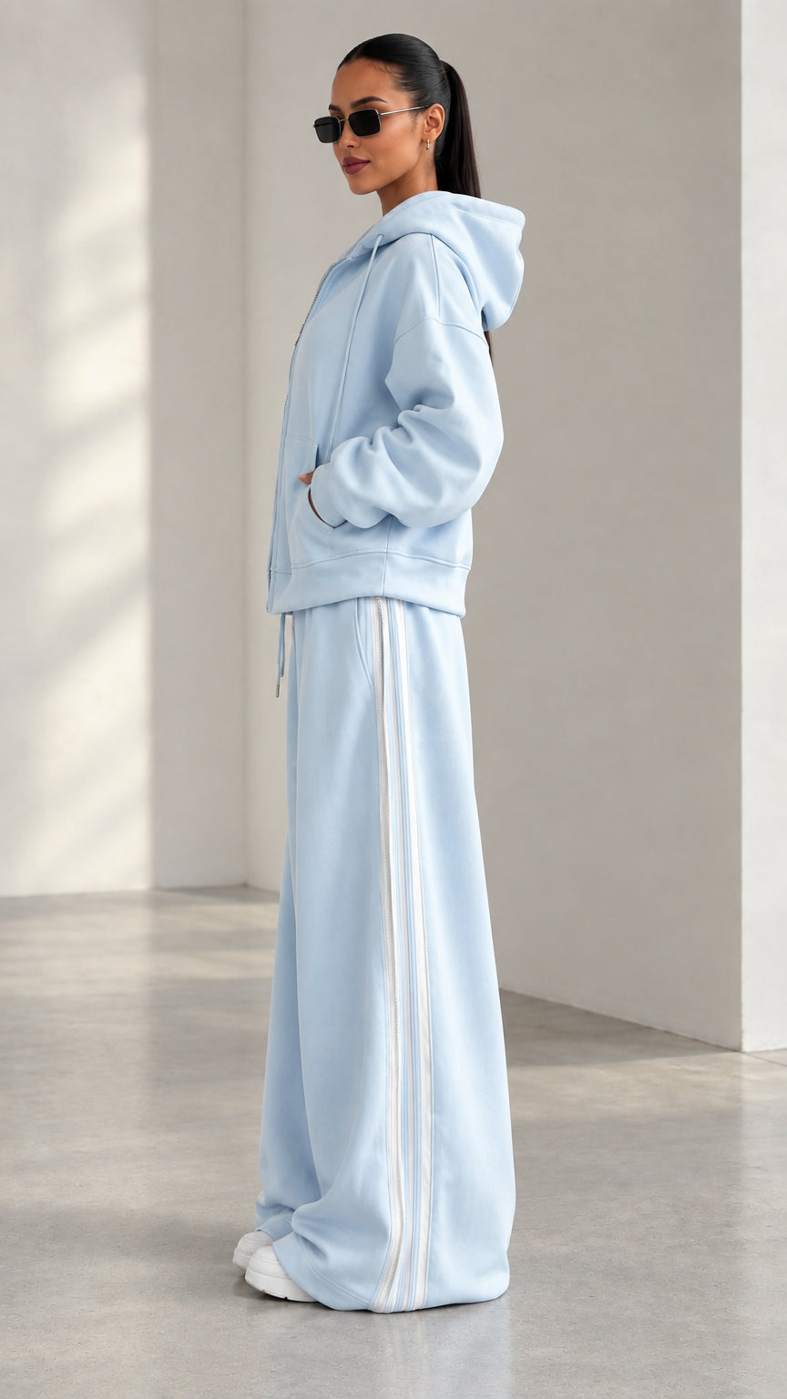 Side angle view of model wearing Light Blue two-piece tracksuit with white side stripes