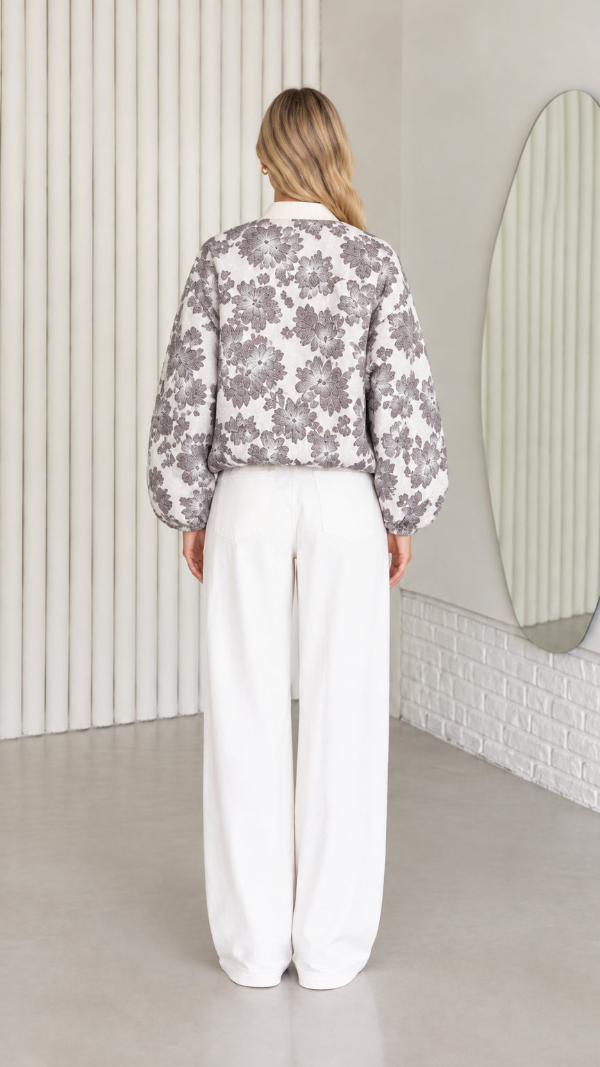 Back view of model wearing charcoal floral bomber jacket and white wide-leg pants