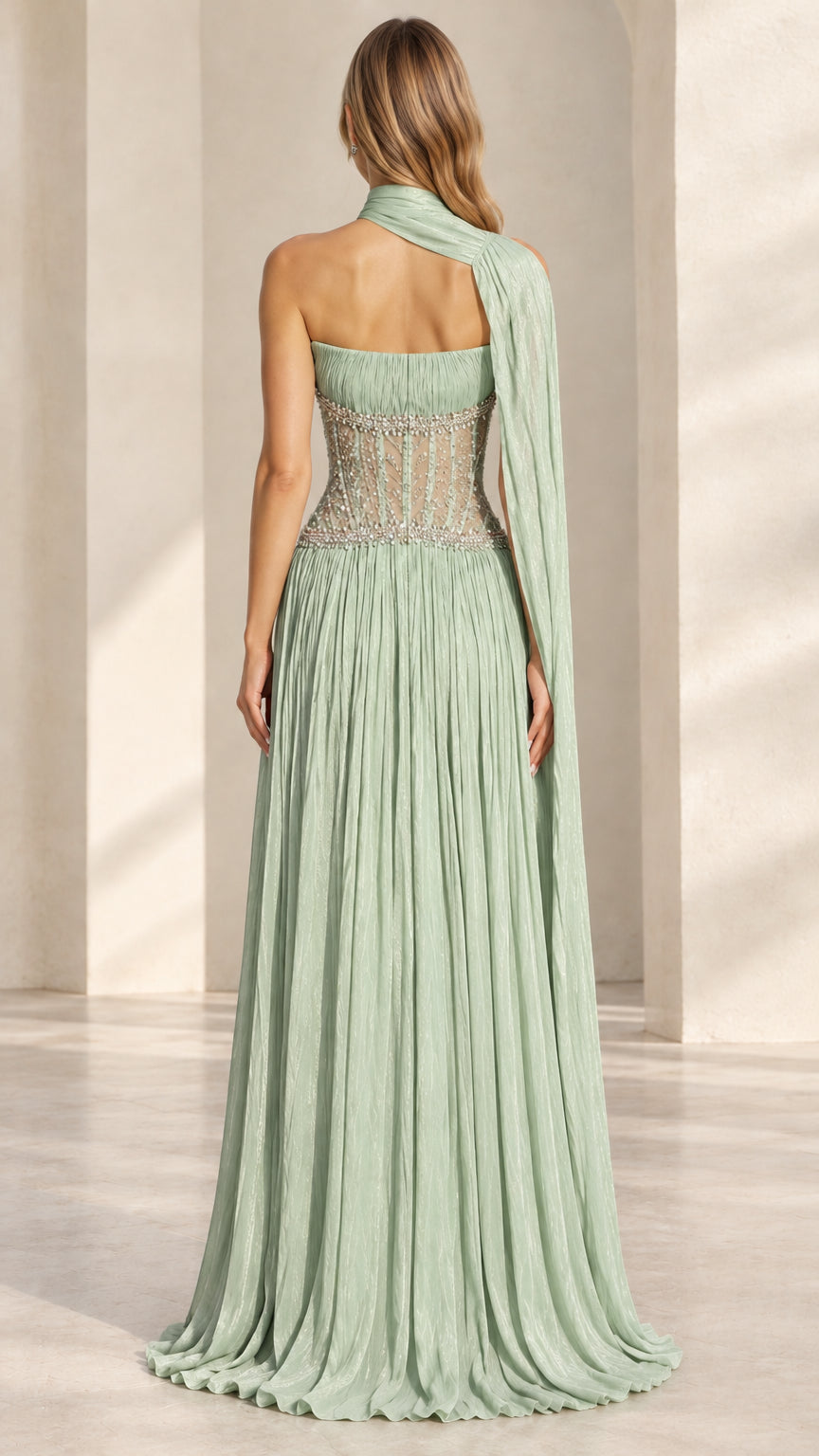 Back view of sage green pleated formal gown with sheer corset and flowing cape