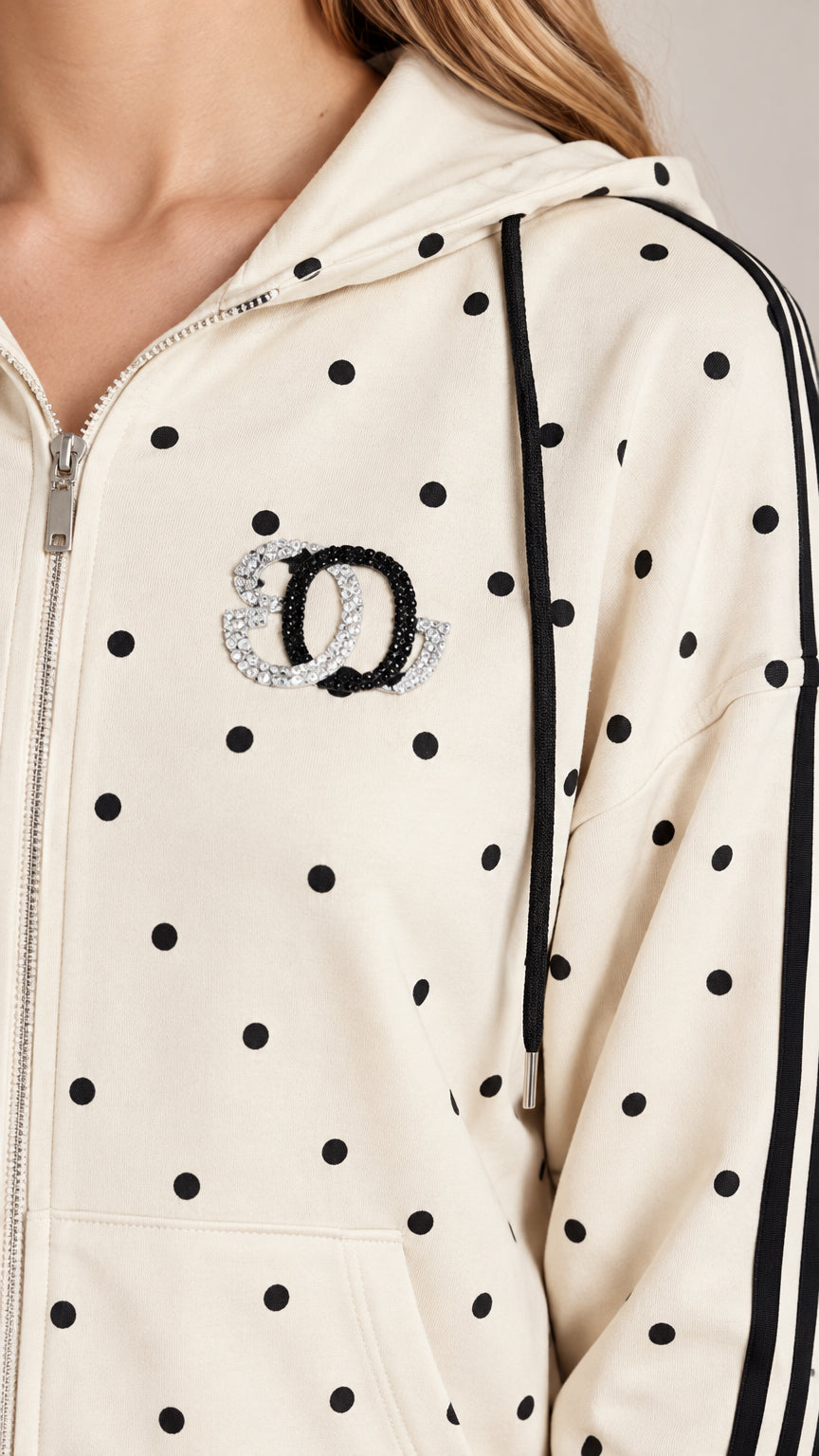Close-up detail of cream polka dot hoodie showing zipper closure, drawstrings, and rhinestone chest emblem