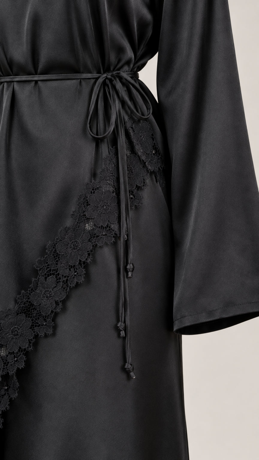 Close-up detail of lace trim, satin fabric, and waist tie cords on black dress