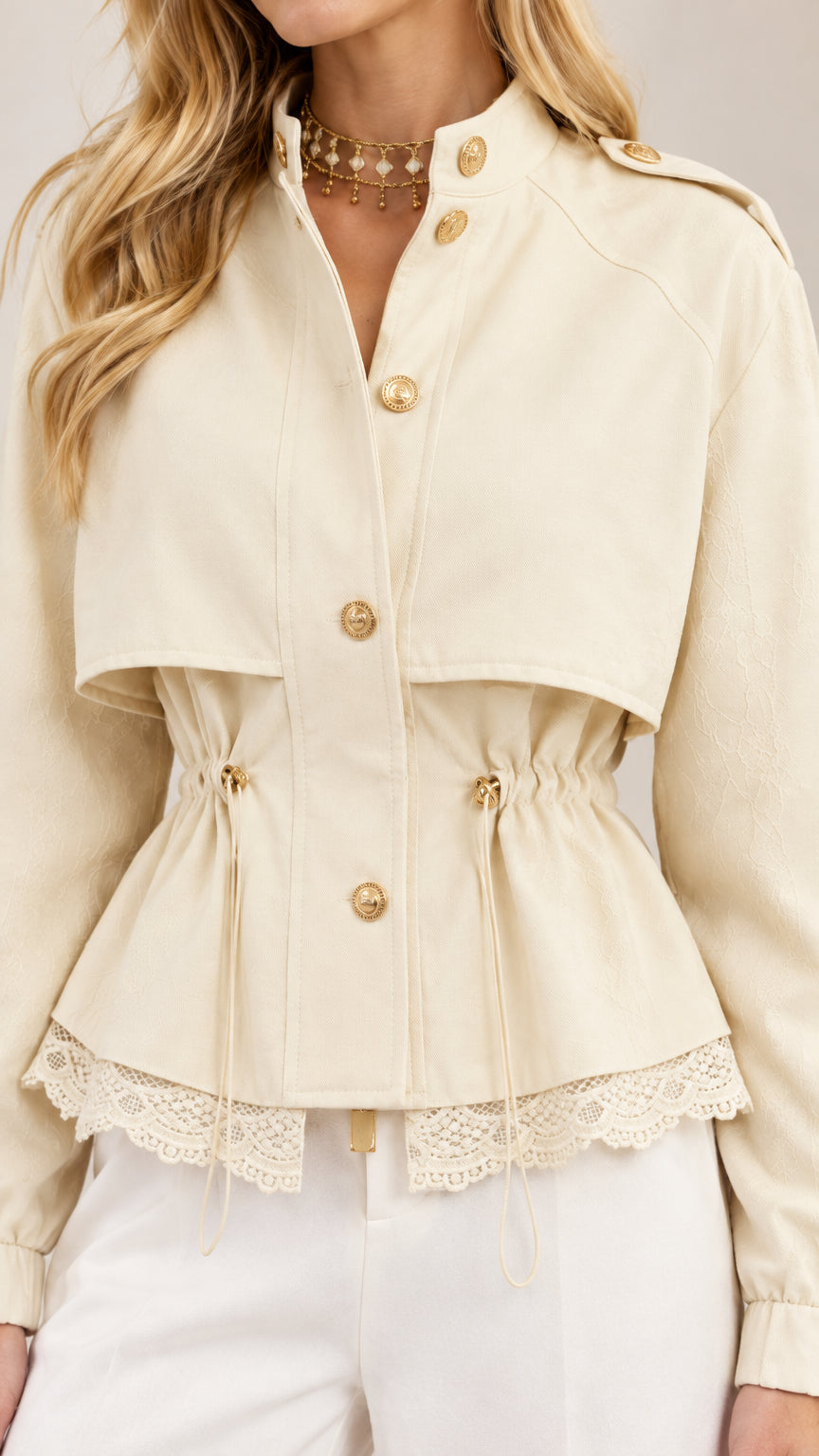 Close-up detail of cream jacket showing gold buttons, drawstring waist, and scalloped lace hem