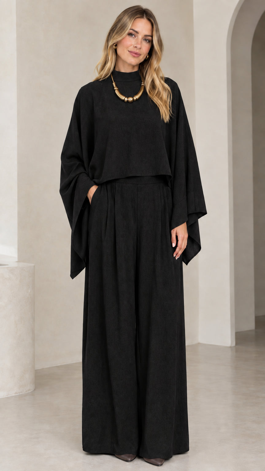 Full-length studio shot of woman wearing black mock neck cape sleeve top and wide leg pants set