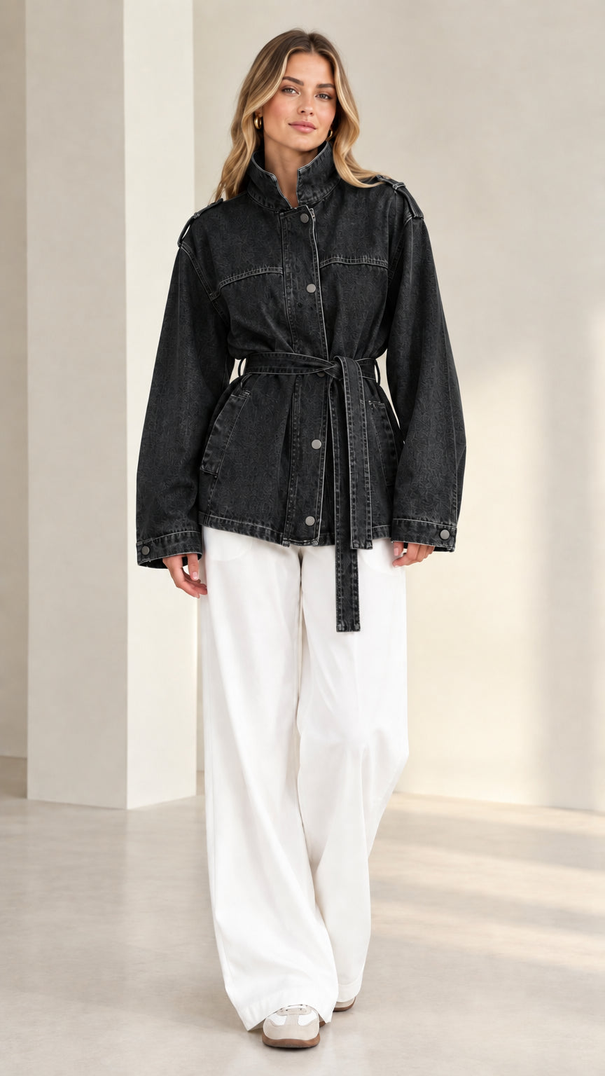 Front view of model wearing washed black belted denim utility jacket with white trousers