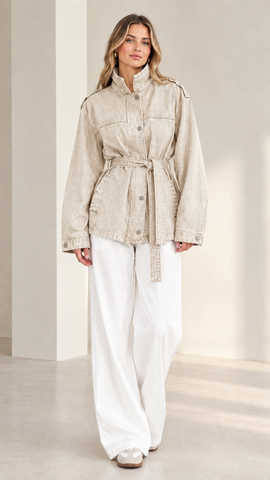 Front view of model wearing beige neutral belted utility denim jacket with white pants